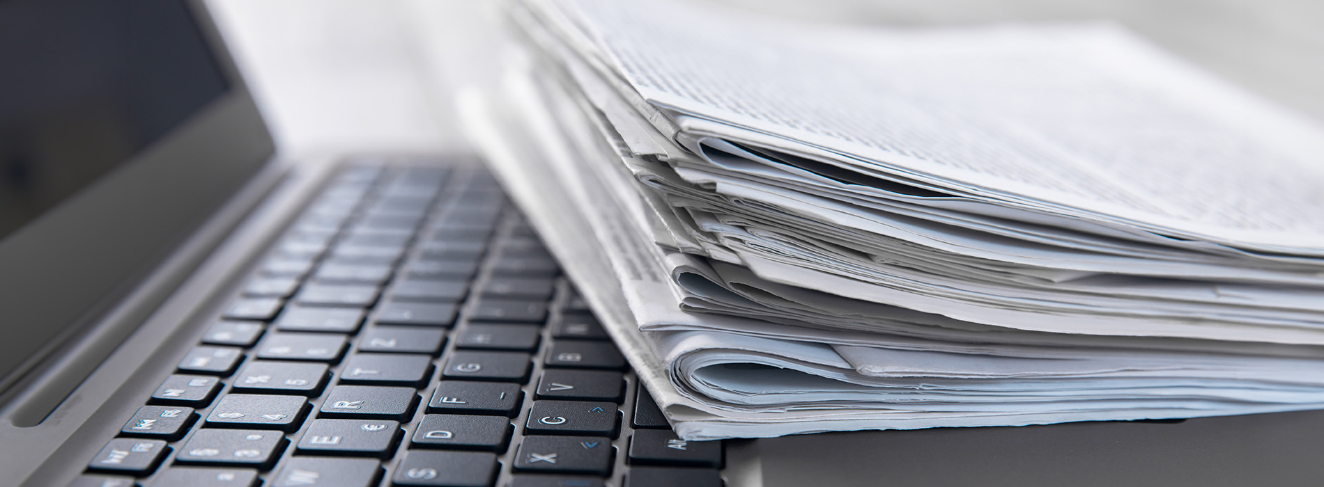 The image shows a stack of papers on top of a laptop keyboard, suggesting a busy work environment with documents being processed or printed.