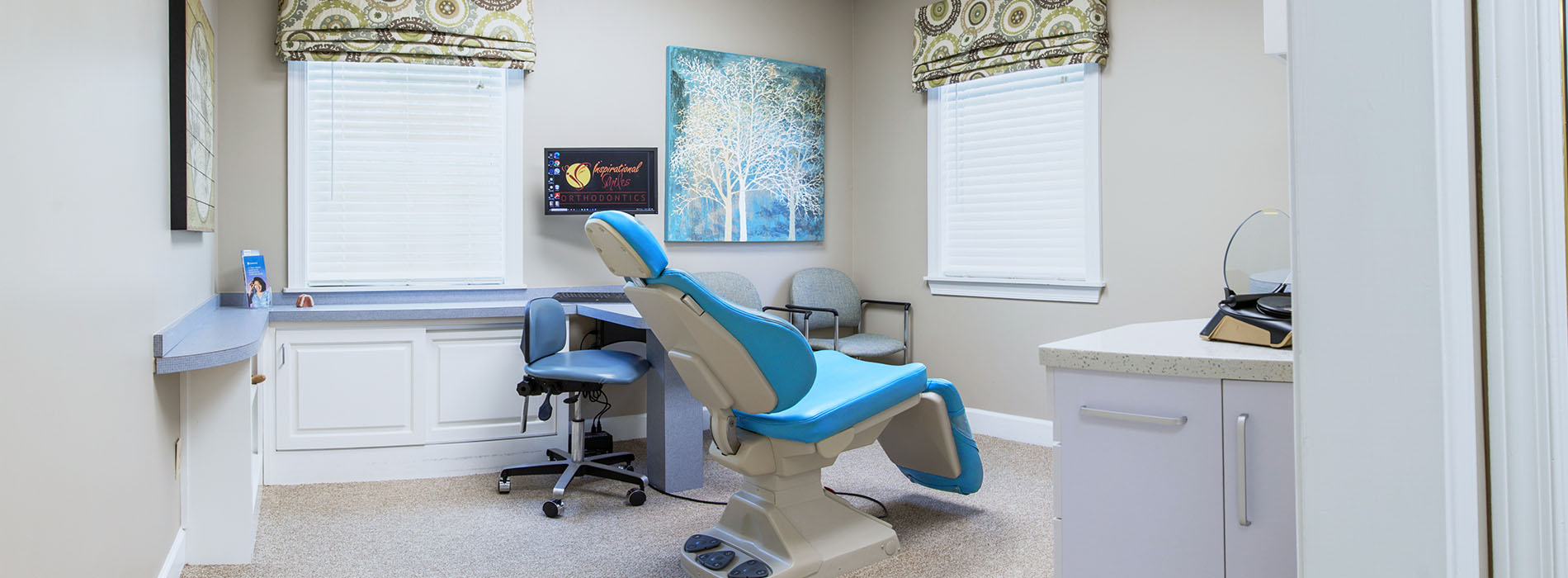 The image shows a dental office interior with a reception area, dental chairs, a computer desk, and a window with blinds partially drawn.